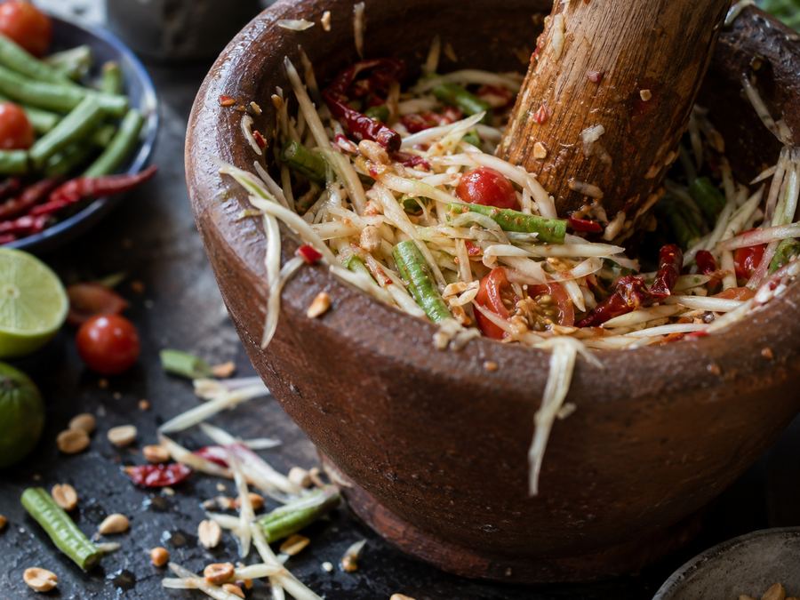Green papaya salad being pounded in a clay mortar